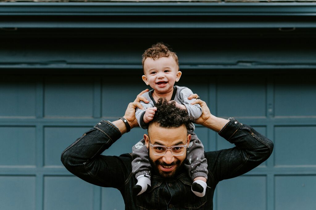 A young father carries his smiling baby on his shoulders