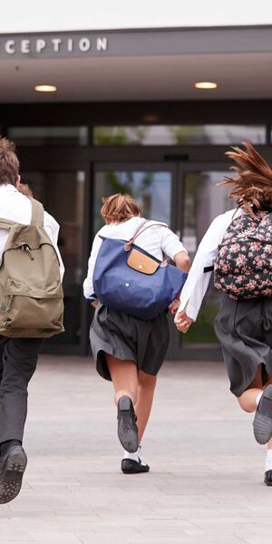 Group of children wearing school uniform and rucksacks running towards school doors