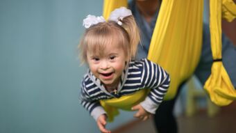 Little girl with Down syndrome held in a yellow sling