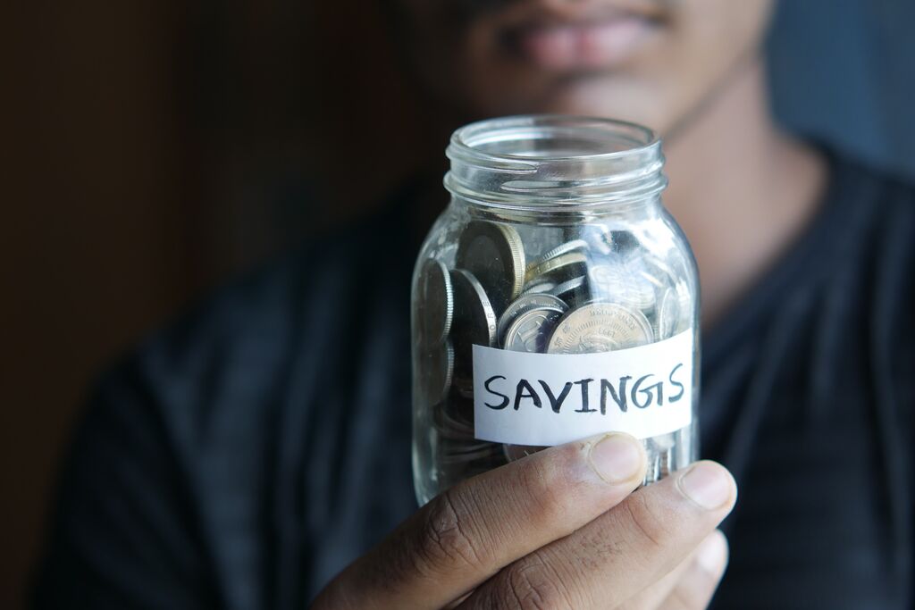 Man holding a jar of pennies with a 'savings' label on it