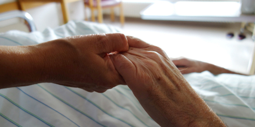 Carer hands holding frail palliative care care home nursing