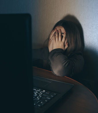 Teenager on computer dark embarrased covering face