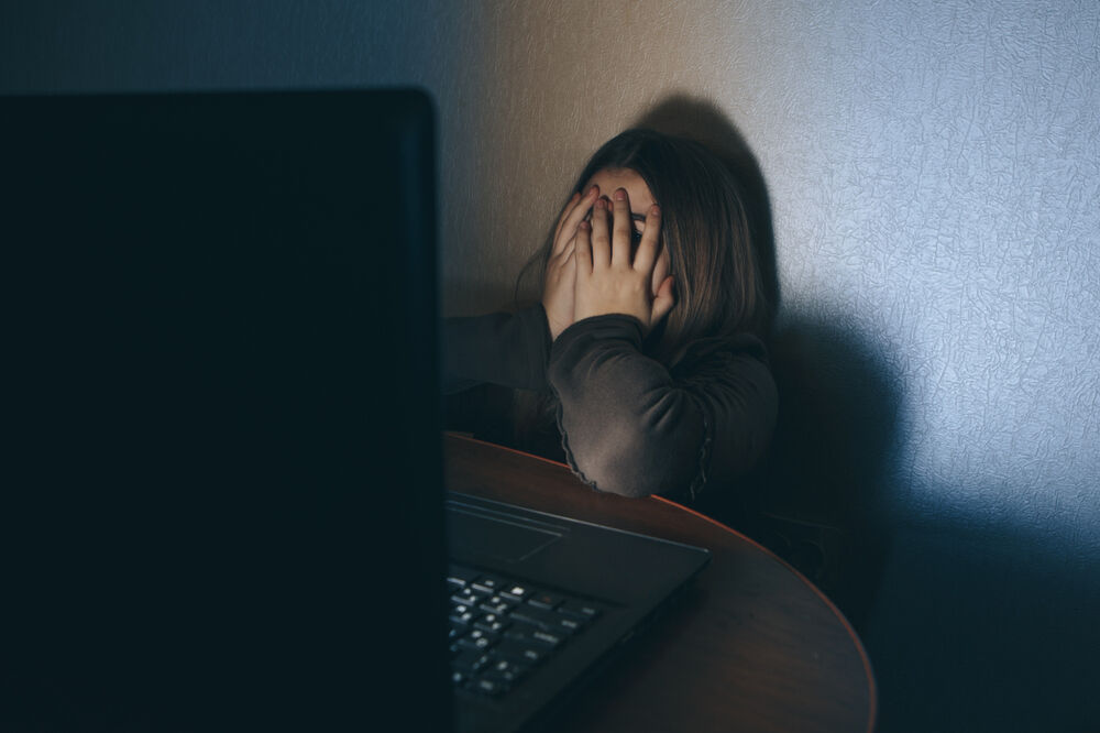 Teenager on computer dark embarrased covering face