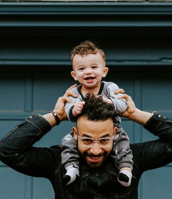 A young father carries his smiling baby on his shoulders