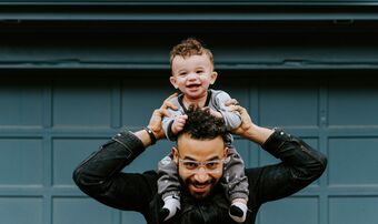 A young father carries his smiling baby on his shoulders